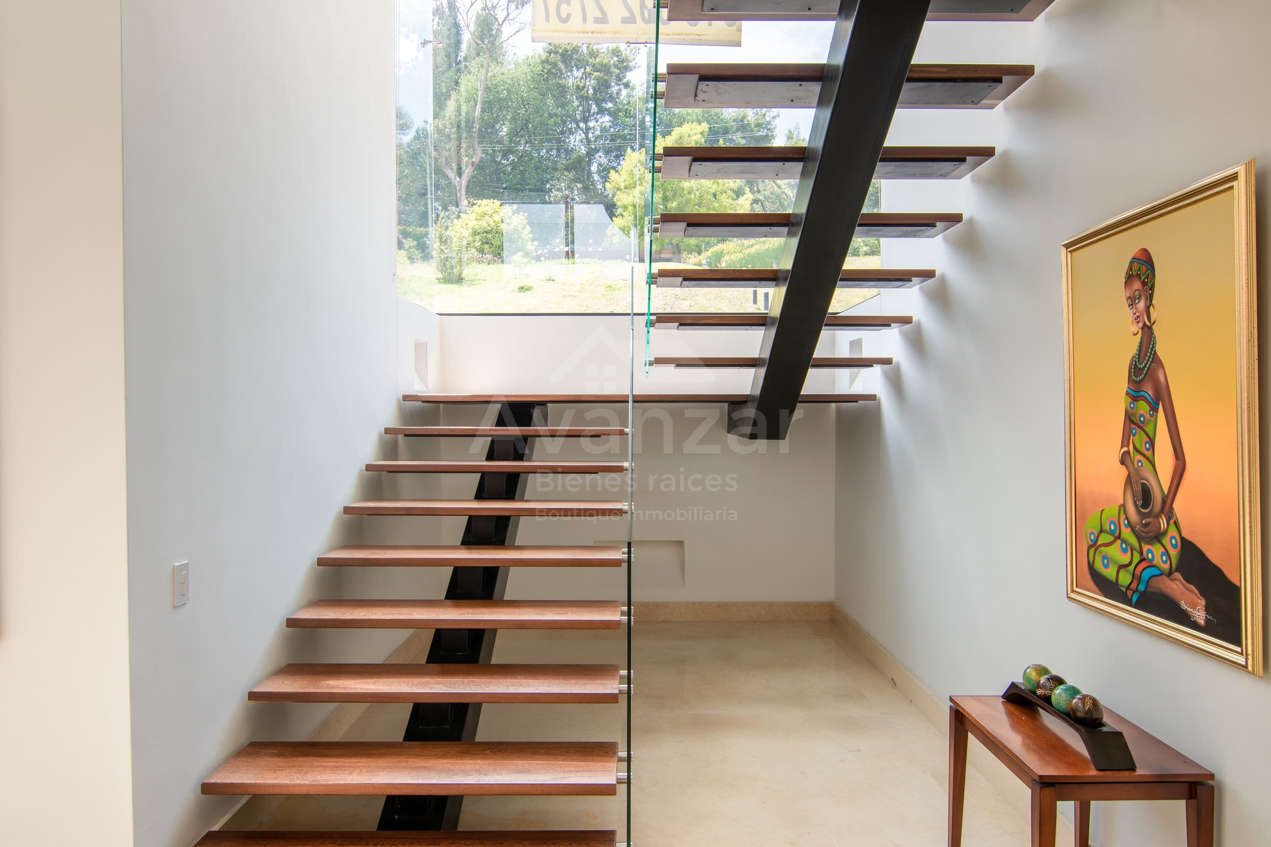 Escalera flotante de madera y vidrio junto a ventanal con vista al jardín