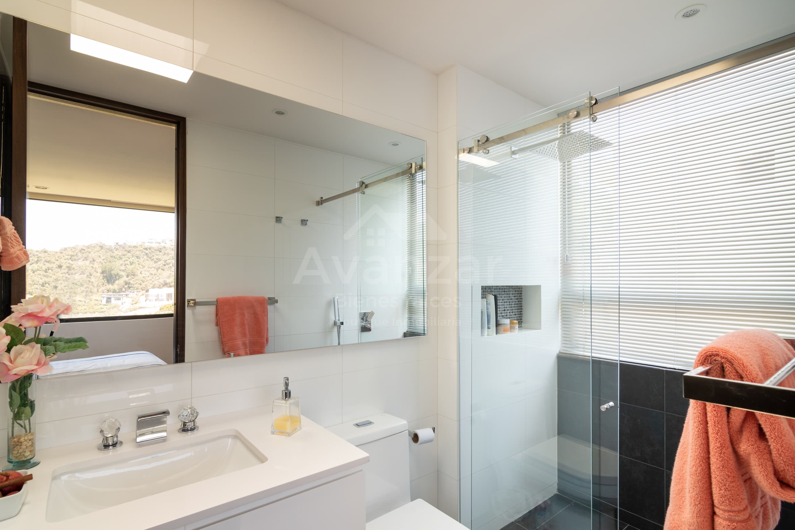 Baño moderno con ducha de vidrio y espejo que refleja la vista boscosa del valle